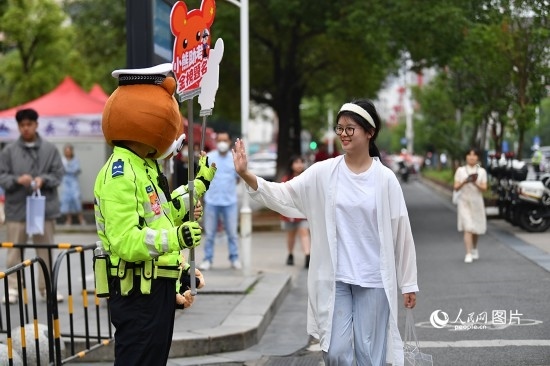 6月7日上午9時(shí)，隨著鈴聲的響起，2023年江西高考正式開考，江西省的53.57萬考生以縣（區(qū)）為單位隨機(jī)安排在全省256個(gè)考點(diǎn)、18968個(gè)考場參加高考。圖為“小熊交警”和考生擊掌鼓勵(lì)。 人民網(wǎng)記者 時(shí)雨攝