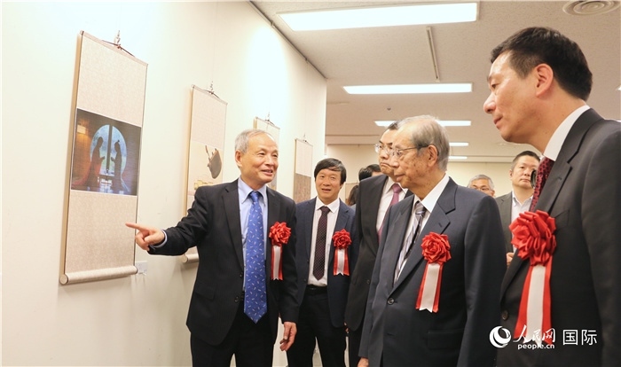 “湖州印象”攝影展主創(chuàng)、世界華人攝影協(xié)會副會長馮學(xué)敏向吳江浩大使、福田康夫前首相等嘉賓介紹展出作品。（人民網(wǎng) 許可攝）