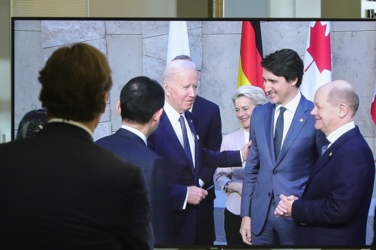 2022年3月24日，在比利時布魯塞爾的北約總部，一名男子觀看屏幕上美國總統(tǒng)拜登（右四）、歐盟委員會主席馮德萊恩（右三）、加拿大總理特魯多（右二）、德國總理朔爾茨（右一）出席七國集團峰會合影儀式的畫面。新華社記者鄭煥松攝