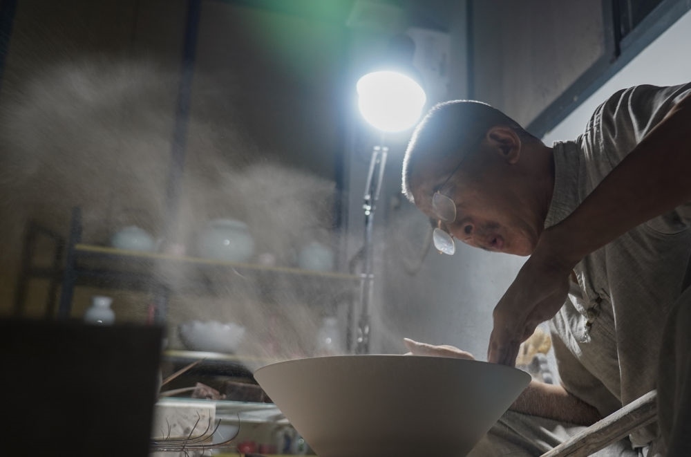 ↑ 在景德鎮(zhèn)，手工匠人吹去坯內(nèi)的泥土（2021年7月14日攝）。