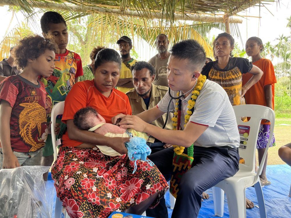 2023年8月5日，在巴布亞新幾內(nèi)亞中央省的一個(gè)村莊里，第12批援巴新中國(guó)醫(yī)療隊(duì)副隊(duì)長(zhǎng)、新生兒科副主任醫(yī)師劉振球?yàn)閶雰禾?lè)聽(tīng)診檢查。泰樂(lè)出生時(shí)患有重癥，一度生命垂危，經(jīng)過(guò)劉振球與當(dāng)?shù)蒯t(yī)護(hù)人員的救治最終痊愈。從2002年起，中國(guó)連續(xù)向巴新派出12批醫(yī)療隊(duì)，為提高巴新醫(yī)療衛(wèi)生水平作出積極貢獻(xiàn)。