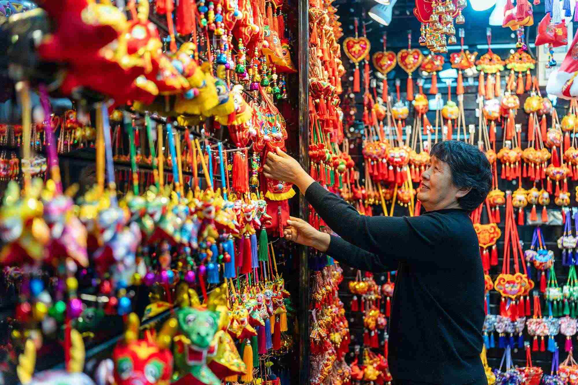 2023年12月11日，金華義烏國際商貿(mào)城，龍年喜慶用品掛滿攤位，顧客正在挑選中。