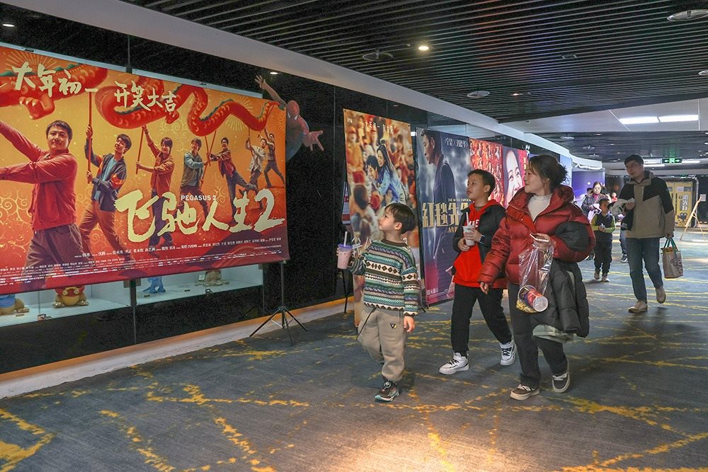 △ 2024年2月16日，在江西贛州一家電影院，觀眾從春節(jié)檔電影的宣傳展板前走過(guò)。