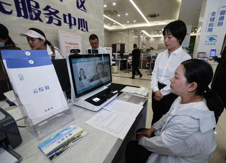 在浙江省嘉興市秀洲區(qū)王江涇鎮(zhèn)便民服務(wù)中心的“跨域通辦·云綜窗”窗口，辦理開業(yè)登記的個體工商戶（右一）通過該系統(tǒng)與江蘇省蘇州市吳江區(qū)盛澤鎮(zhèn)行政審批局工作人員視頻連線，進(jìn)行身份讀取及材料線上審核（2024年5月9日攝）。新華社記者 徐昱 攝