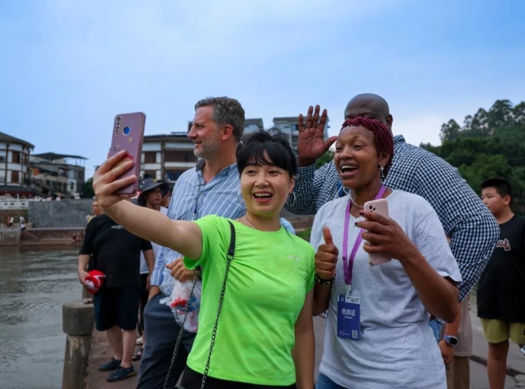 2024“一帶一路”媒體合作論壇聯(lián)合采訪調(diào)研行成員在樂山蘇稽古鎮(zhèn)與游客合影留念。本報(bào)記者 伊霄攝