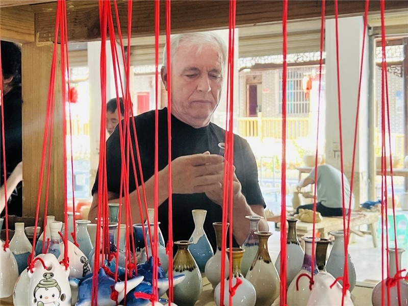 鄉(xiāng)愁如同一根根紅線，將游子與故鄉(xiāng)永遠(yuǎn)地牽連到一起?；逄账囄幕瘎?chuàng)意一條街的母氏陶藝館內(nèi)，紅線吊著陶瓶，思緒游走萬里。摩爾多瓦“信息標(biāo)簽”通訊社社長亞歷山大·塔納斯端詳著館內(nèi)展示的陶藝作品，并挑選出心儀的小擺件帶回摩爾多瓦，也帶走花茂村的“鄉(xiāng)愁”。（張亞欣攝）