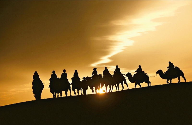 新時(shí)代以來(lái)，文化和旅游深度融合發(fā)展體制機(jī)制不斷健全，成功走出了一條獨(dú)具特色的中國(guó)旅游發(fā)展之路。圖為2024年9月1日清晨，游客在甘肅省敦煌市鳴沙山月牙泉景區(qū)乘騎駱駝，欣賞大漠風(fēng)光，體驗(yàn)絲路風(fēng)情。 新華社發(fā) 張曉亮/攝