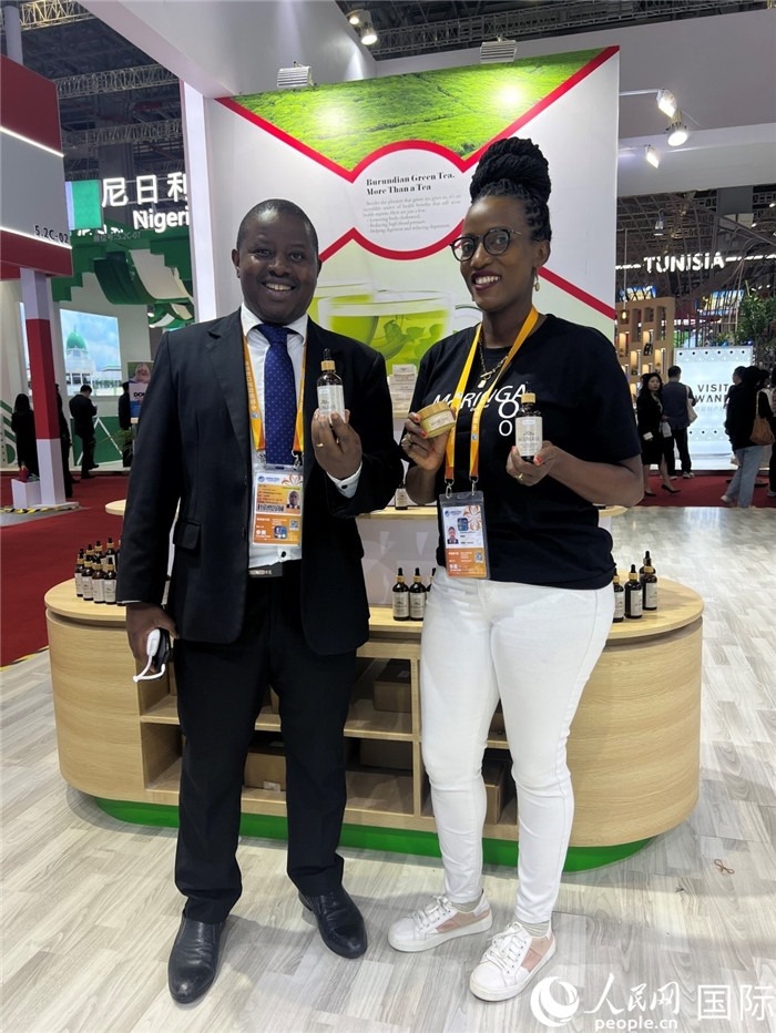 6月6日，布隆迪駐華大使館一等參贊布利馬索·阿爾弗雷德 (左，Bulimaso Alfred) 和參展商卡馬里扎·埃斯特拉 (Kamariza Estella) 在第七屆中國國際進口博覽會布隆迪館展示當?shù)厣a(chǎn)的辣木油。（人民網(wǎng) 艾里士 攝）
