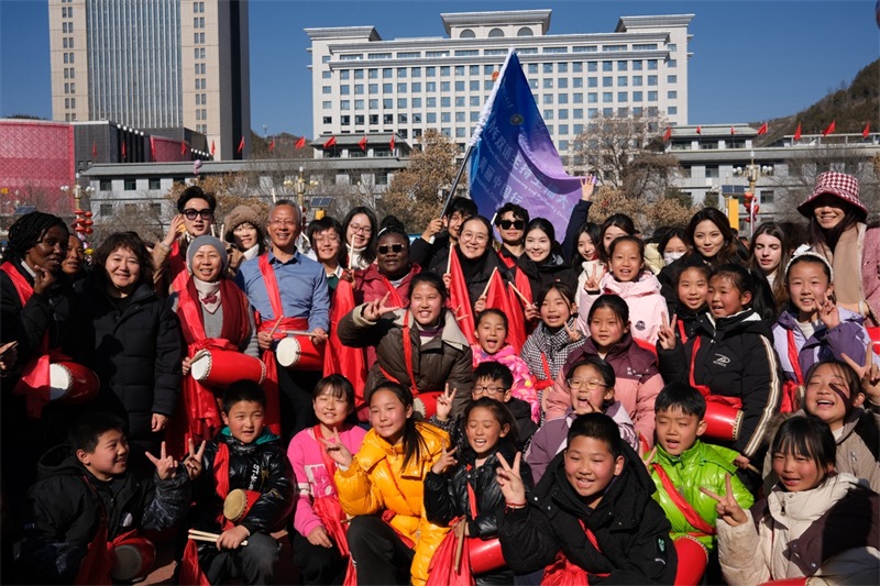 中外青年學子在安塞文化廣場觀看陜北腰鼓和大秧歌表演后合影留念，大家踏著鼓點共舞，翻飛的紅綢與躍動的身影交織，在黃土地廣場上繪出一幅生動的陜北民俗互動畫卷